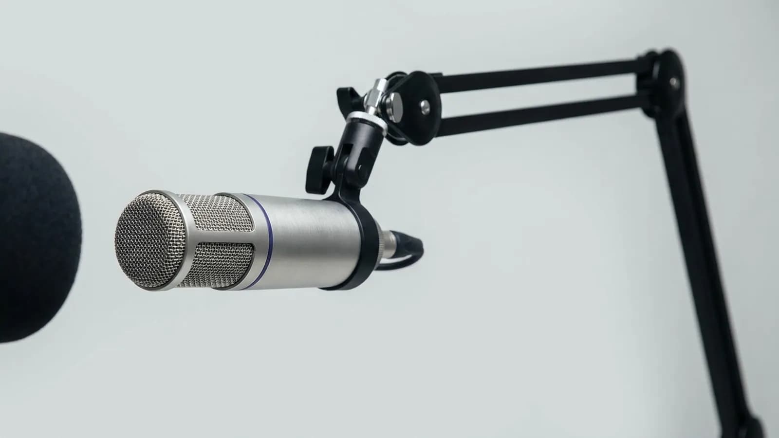 A studio condenser microphone on a boom arm against a grey backdrop