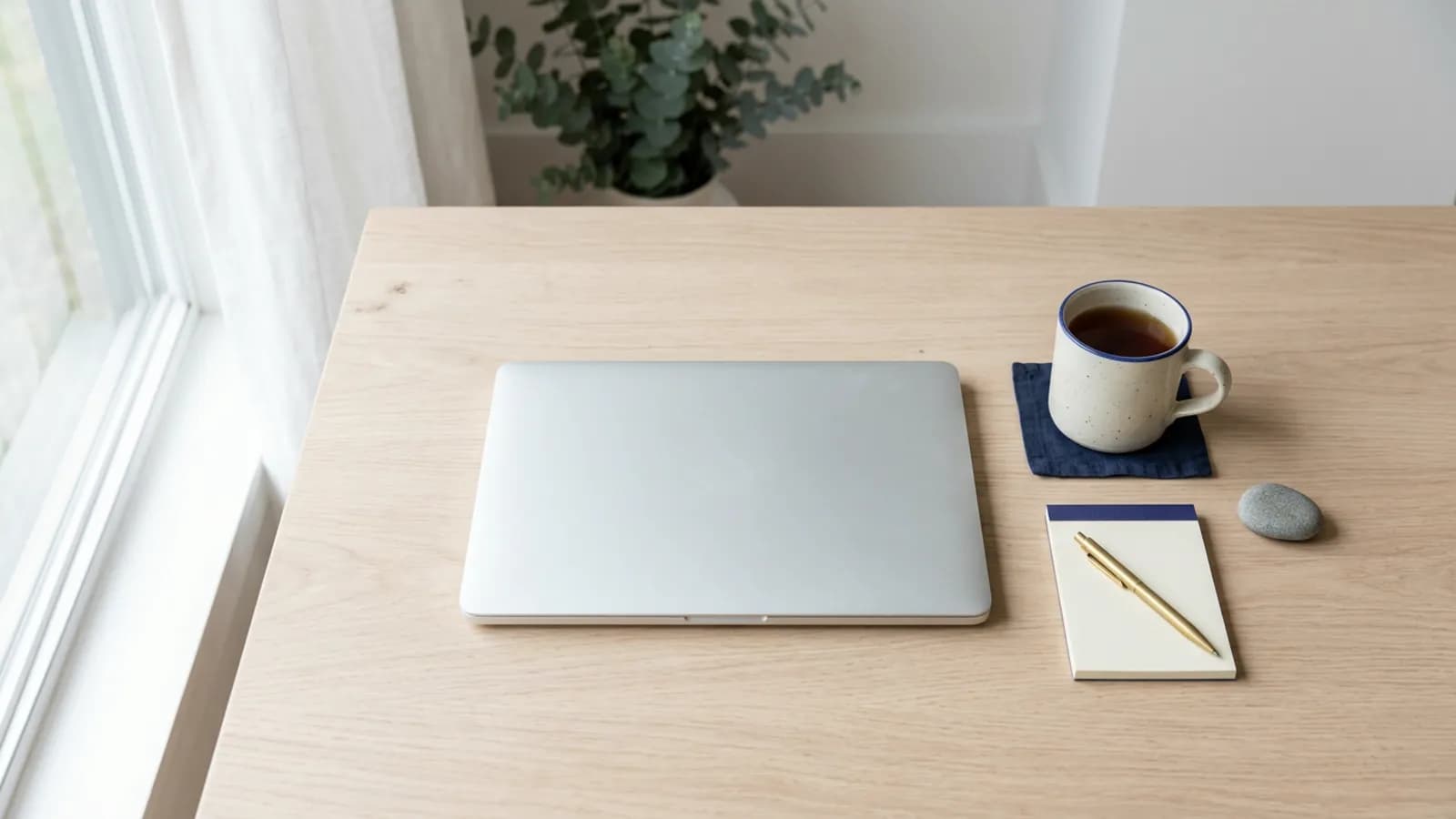 A tidy desk from above with a closed laptop and a mug