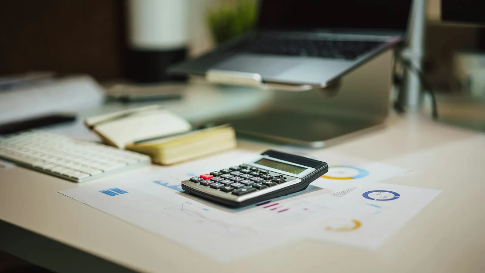 A pocket calculator resting on printed charts in front of a laptop on a desk