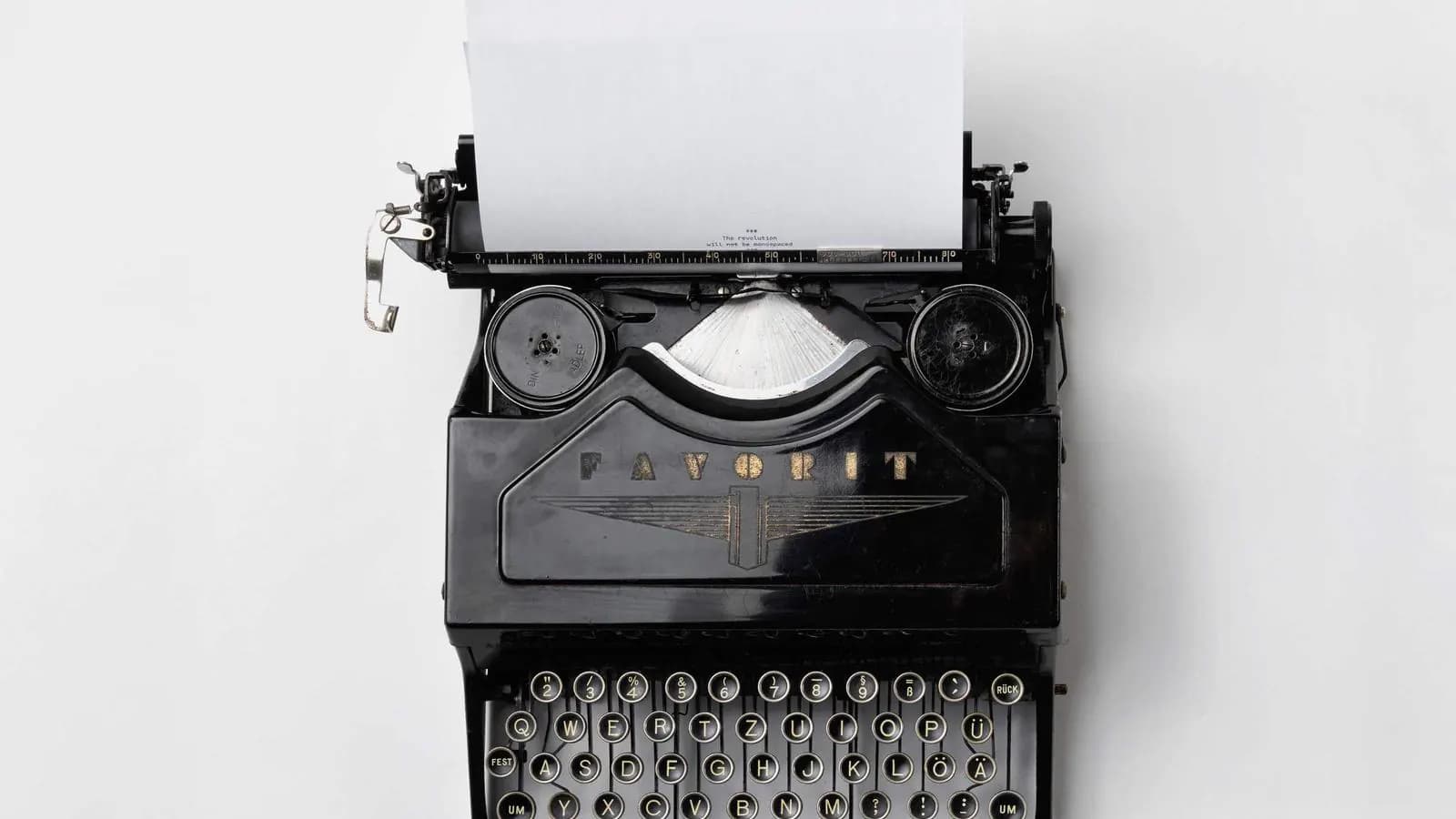 A black typewriter with a blank sheet of paper loaded, photographed from above on white