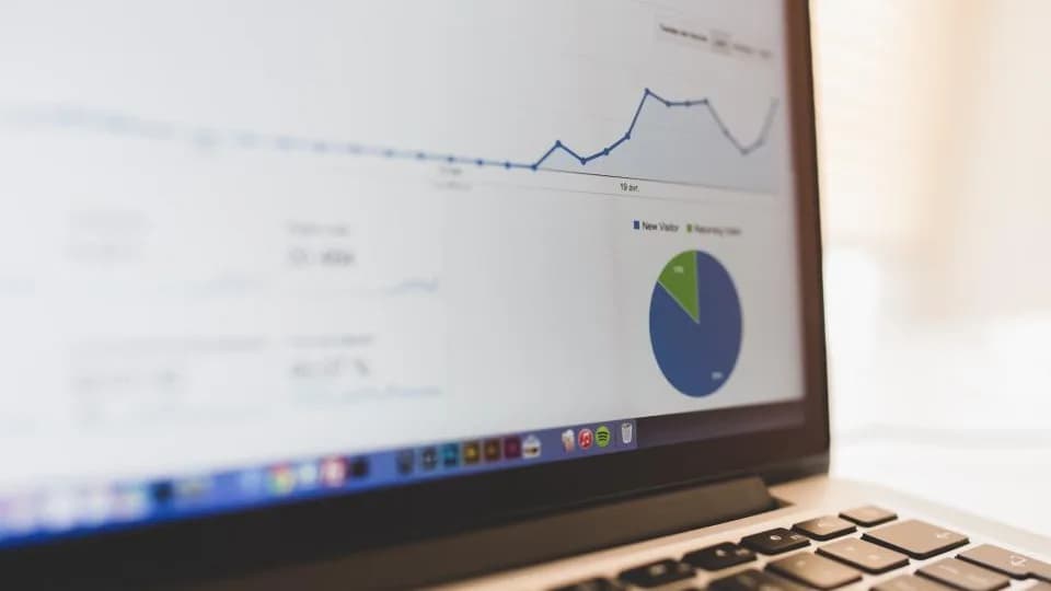 A laptop on a desk showing a web analytics dashboard with a line graph and a pie chart