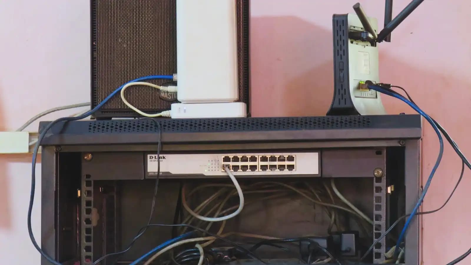 A wall-mounted network rack holding a sixteen-port switch, a router and a tangle of Ethernet cables