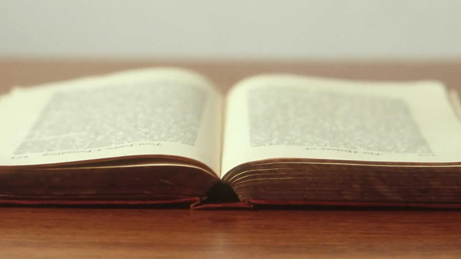 An old hardback book lying open on a polished wooden table, its printed pages softly out of focus