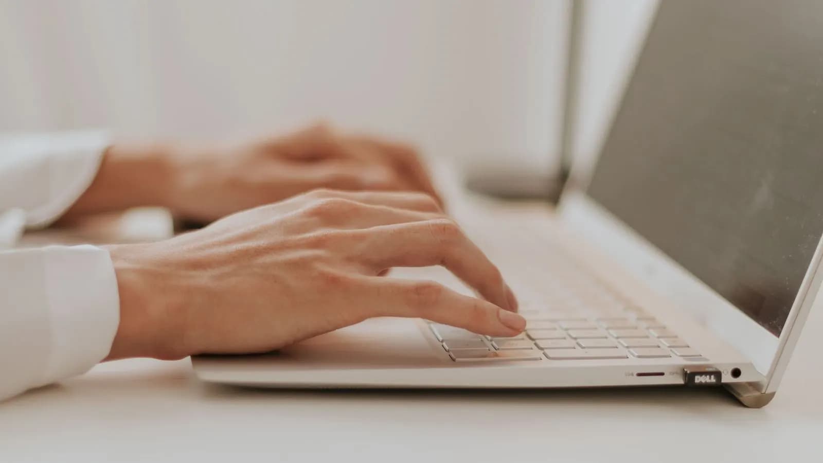 Close-up of a person's hands on a silver laptop keyboard at a bright desk