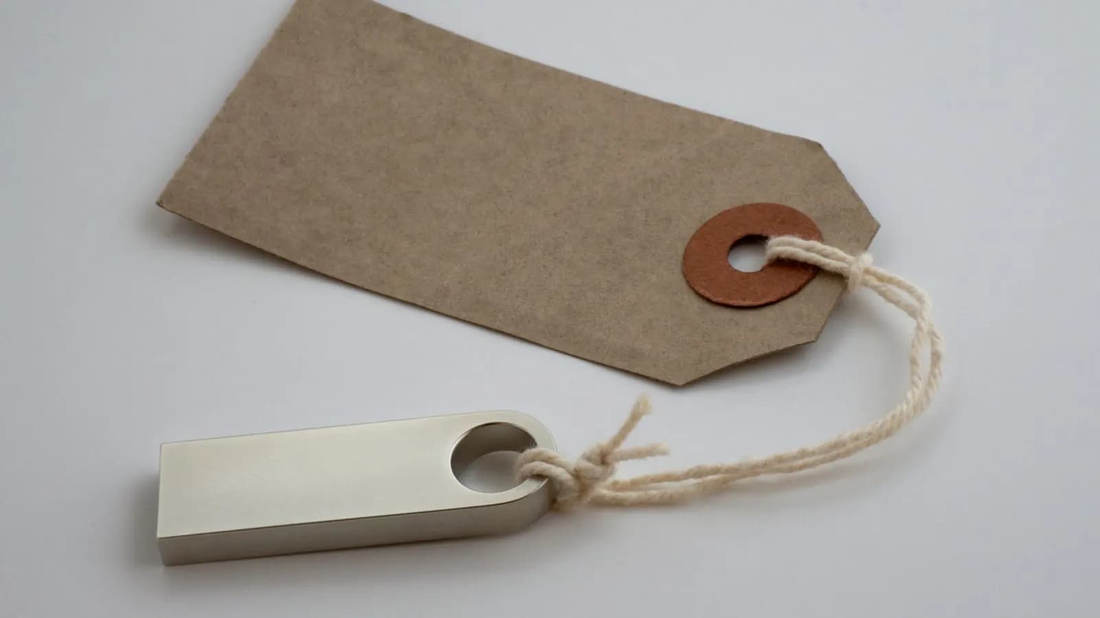 A blank brown price tag tied with string to a small silver USB stick on a white surface