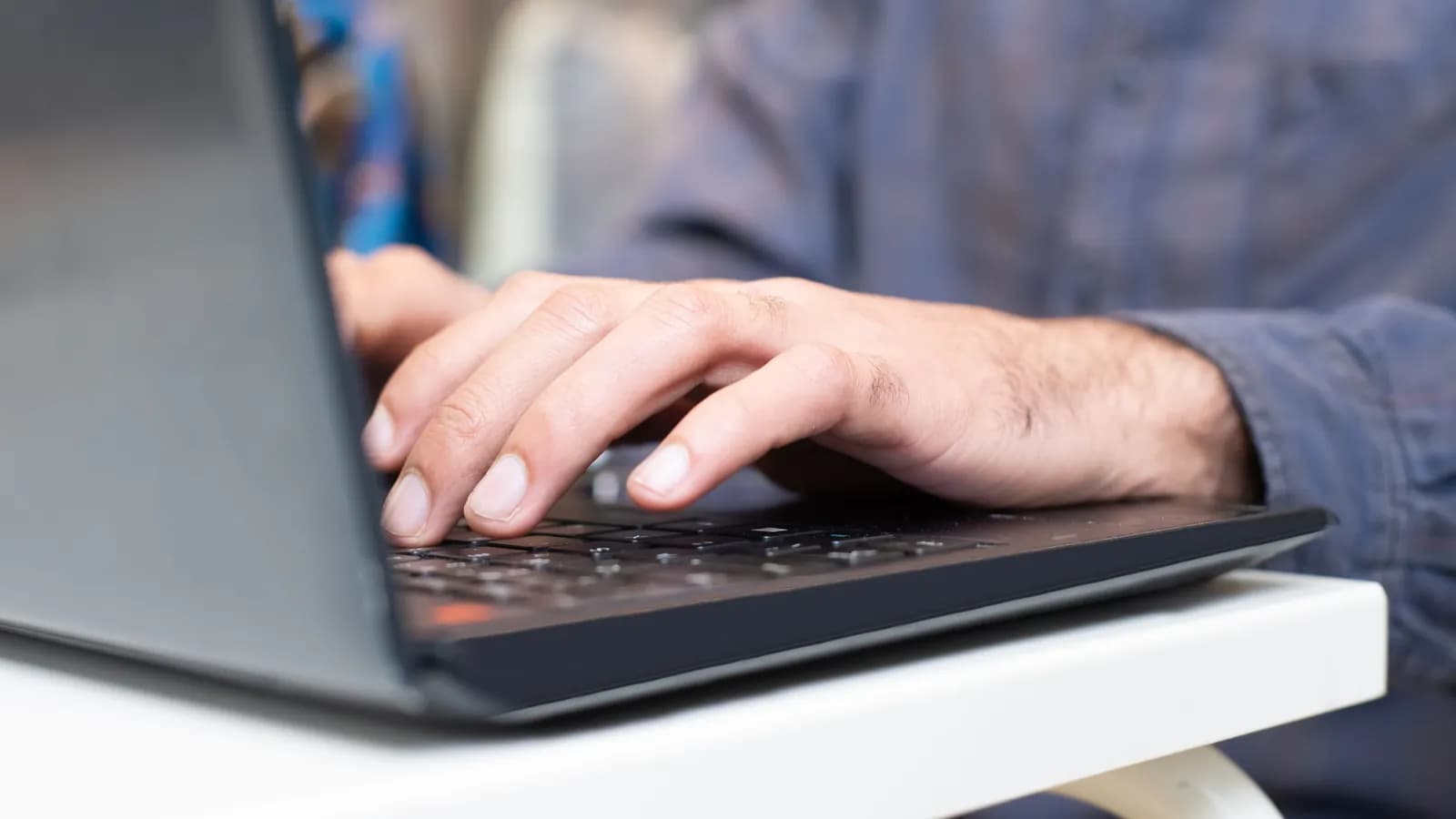 Photograph: a close-up of one hand resting on a laptop keyboard mid-sentence, the rest of the desk out of focus