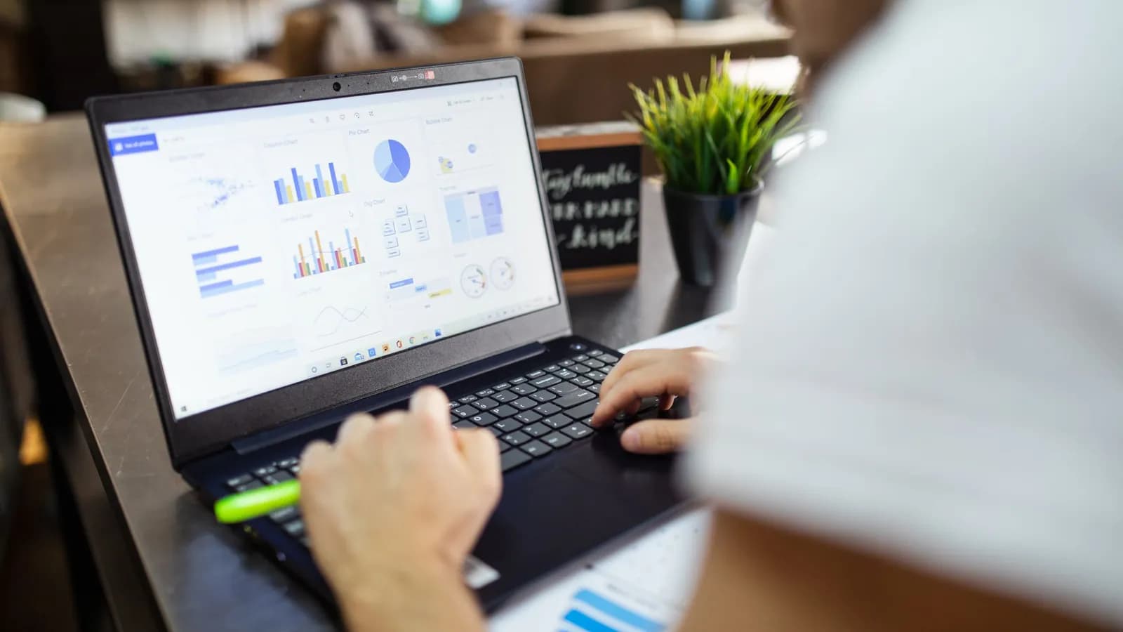 Photograph: over the shoulder of someone typing at a laptop, the screen filled with a grid of small charts and figures
