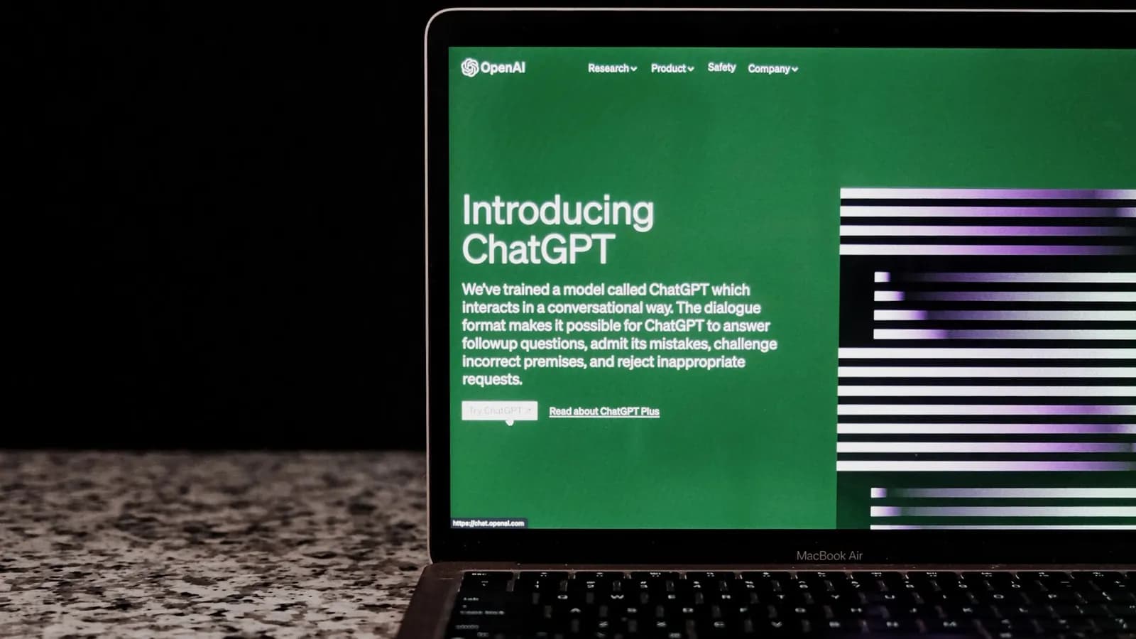 Photograph: a laptop on a speckled worktop showing OpenAI's ChatGPT announcement page, the screen the only lit thing in a dark room